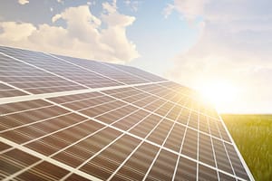 Solaranlage bei Sonnenuntergang auf einer grünen Wiese unter blauem Himmel mit weißen Schäfchenwolken - Pangea Life