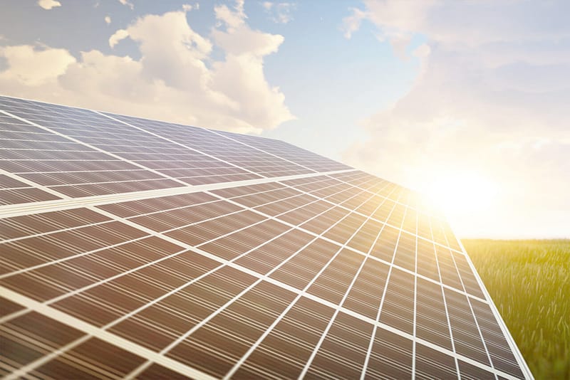 Solaranlage bei Sonnenuntergang auf einer grünen Wiese unter blauem Himmel mit weißen Schäfchenwolken - Pangea Life