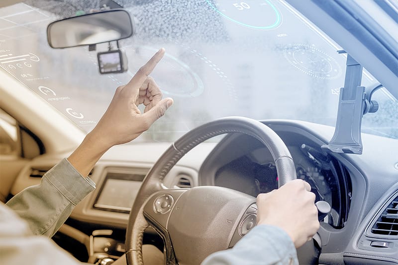 Innenansicht eines autonomen Fahrzeugs mit digitalen Projektionen auf der Windschutzscheibe und einer Hand, die die Touch-Steuerung nutzt – dargestellt im Kontext der Ethik der Technologieinvestitionen.